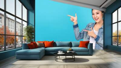 Banner of Happy asian woman standing pointing hands to copyspace on blue background. Cute asia girl smiling wearing casual jeans shirt and finger pointing to aside for present promotions. Wall mural