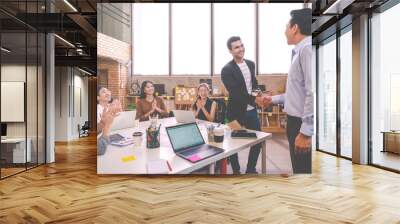 Candid of Indian creative design man smiling and shaking hands with coworker man or colleague and other clapping hand at office workplace. Introduction to team or marketing group concept soft tone. Wall mural