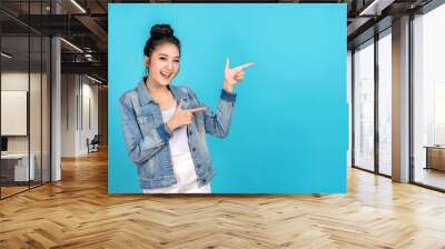 Happy asian woman feeling happiness and standing pointing hands to copyspace on blue background. Cute asia girl smiling wearing casual jeans shirt and finger pointing to aside for present promotions. Wall mural