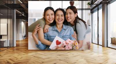 Happy time Mother day grown up child looking at camera cuddle hug give flower gift box red heart card to mature mum. Love kiss care mom asia middle age adult people smile enjoy sitting at home sofa. Wall mural