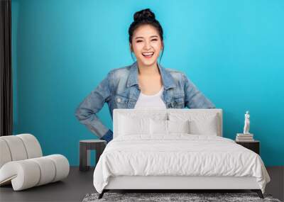 Portrait of Happy asian woman standing and feeling happiness and confident on blue background. Cute asia girl smiling or laughing wearing casual travel uniform in jeans shirt and keeping hands on hips Wall mural