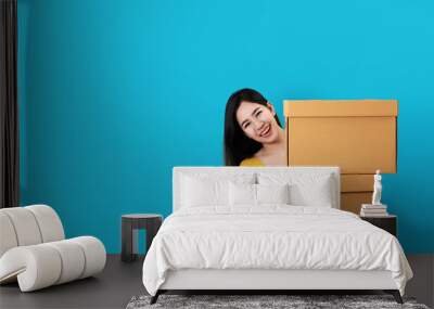 Portrait of young asian entrepreneur happy smiling and holding or carrying pile of boxes in hands with blue isolated background and copy space. Asian woman move to new home or ecommerce owner concept. Wall mural