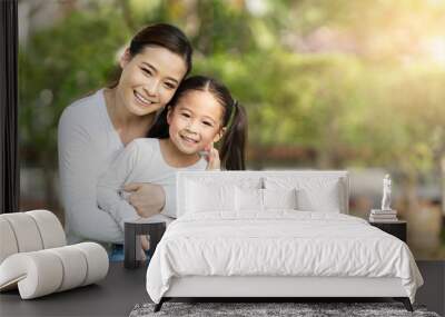 Portrait of young happy asian mother and little cute daughter smiling, sitting and looking at camera at outdoor public nature park with copy space in family bonding and casual relax lifestyle concept. Wall mural