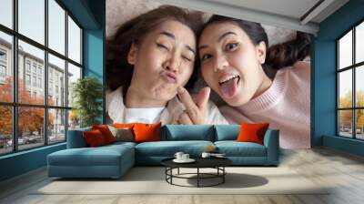 POV attractive beautiful two people asia young lady girl use mobile phone take photo picture video overjoy lying down at home floor have good time day together quarantine in mum healthy health care. Wall mural