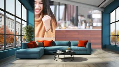 Young attractive asian student using or looking at laptop computer smiling with success at cafe coffee shop. Asian woman or happy entrepreneur gesture hand success with copy space banner concept. Wall mural