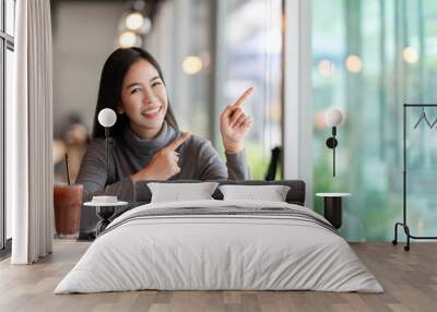 Young attractive asian woman pointing up to side for showing message feeling happy amazed at cafe coffee shop background with copyspace. Blogger, entrepreneur, customer or social influencer concept. Wall mural