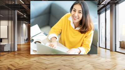 Young attractive happy asian female student sitting at living room floor smiling and looking up at camera working on laptop at home office. Young startup entrepreneur or freelance business concept. Wall mural