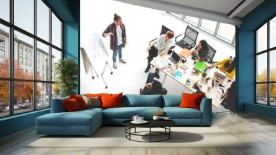 Young caucasian creative man standing and making presentation at modern office happy talking and brainstorming with team. Casual multiethnic people business meeting concept with wide angle top view. Wall mural