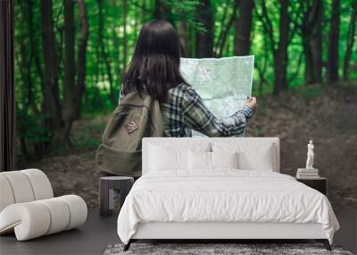 Young woman with backpack and map on forest path on summer day. Girl with tourist backpack travels. Wall mural