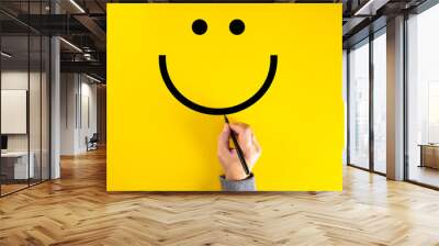 Male hand drawing a smiling happy face sketch on yellow background. Client satisfaction. Wall mural