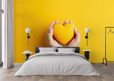 Female hands on a yellow background holding a yellow heart. The concept of donations and family insurance, World Heart Day. Valentine's Day. Wall mural