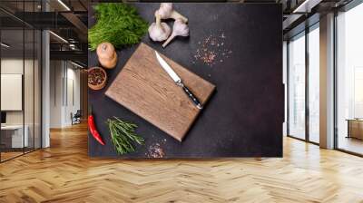 A wooden cutting board with spices, herbs, cherry tomatoes and salt on a black concrete background Wall mural