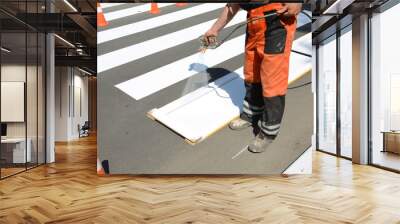 Worker is painting a pedestrian crosswalk. Technical road man worker painting and remarking pedestrian crossing lines on asphalt surface using paint sprayer gun. Wall mural