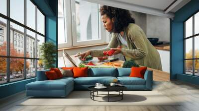 A woman reading a recipe and cooking in the kitchen Wall mural