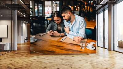 couple using mobile phone while drinking coffee in cafe Wall mural