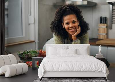 Front view of a mixed race woman leaning on a kitchen table with vegetables on it Wall mural