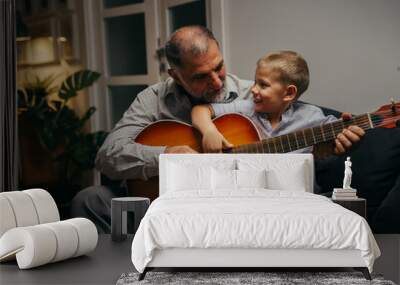 grandfather with his grandson sitting on sofa and playing guitar at home. evening scene Wall mural