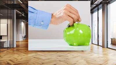 Mans hand putting coin into green piggy bank Wall mural