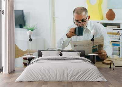 middle age man sitting at the dinning table, having breakfast and reading newspaper at home Wall mural