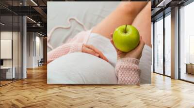 Pregnant woman eating apple. Aerial close up view. Wall mural