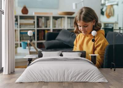 teenage girl using tablet computer while sitting on sofa in living room Wall mural