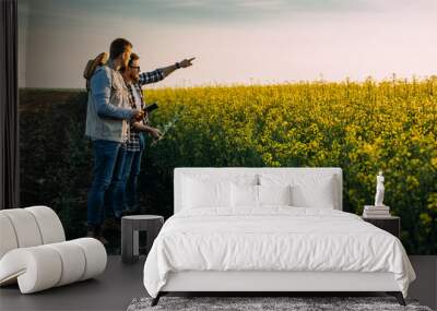 Two brothers are standing on their farmland and inspecting a field of oilseed rape. Wall mural