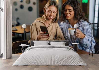 Two women looking at phone in a cafe Wall mural