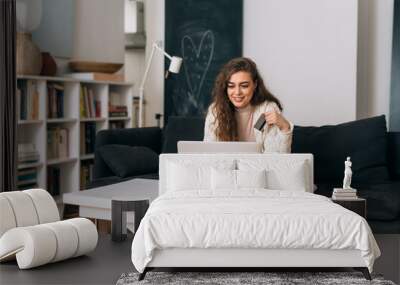 woman shopping online on laptop computer while sitting on sofa in her home Wall mural