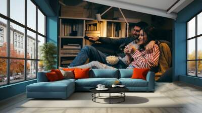 young couple watching television together at home Wall mural