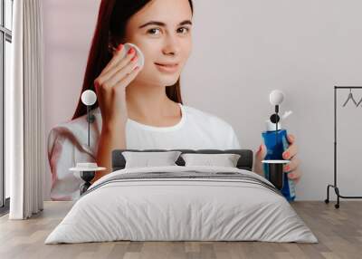 Makeup remove skin care. Closeup woman holding cotton swab and makeup remover liquid in hands. Woman cleaning her face with lotion and cotton pad. Wall mural