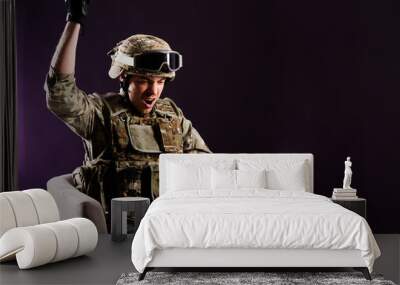 Man gamer with laptop is celebraiting the win in soldier clothes on brown background. Concept of win. Wall mural