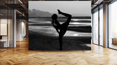 silhouette of a girl doing gymnastics on the beach by the sea with one leg in black and white effect Wall mural