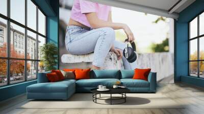 A young attractive woman with curly hair sitting outdoors with headphones in her hands and chilling. Wall mural