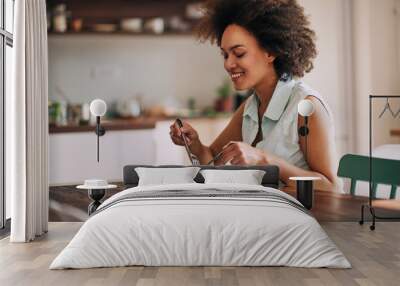 Beautiful mixed race woman eating pasta for dinner while sitting at kitchen table. Wall mural