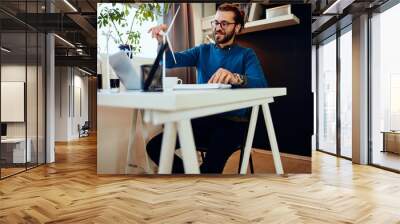 Handsome bearded caucasian entrepreneur sitting in his office and working on important project. Sustainable concept. Wall mural