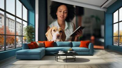 Mixed race woman petting her dog and using tablet while sitting on the floor. Wall mural