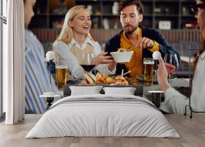 Multiethnic friends sitting at restaurant, drinking alcohol, chatting and having burgers for dinner. Wall mural