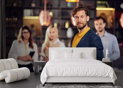 Portrait of young bearded Caucasian businessman dressed smart casual posing with his successful team in restaurant. Wall mural