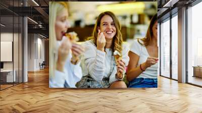 Three happy girls are sitting at a restaurant, chatting and eating ice cream after shopping. Wall mural