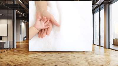 Baby little hand on mom's hand against white sheets background Wall mural