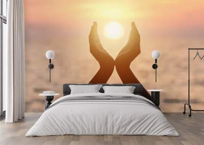 June summer sun solstice concept with silhouette of happy young woman's hands relaxing, meditating and holding sunset against warm golden hour sky on the beach with natural ocean or sea background Wall mural