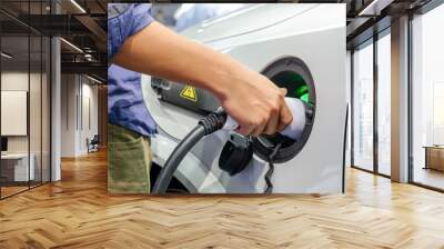 Close-up asia men hands who are fueling a new vehicle electrification via rechargeable electricity machine, Electric cars are a new innovation in the future, built to replace cars powered by oil. Wall mural