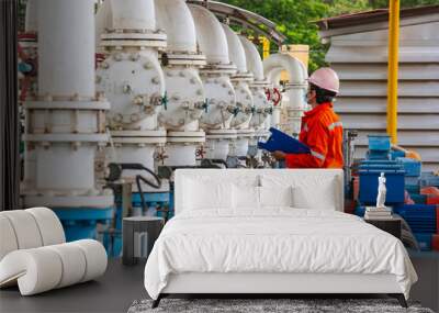 Male worker inspection pump motor oil at steel long pipes and pipe elbow in station oil factory during refinery valve of visual check record pipeline Wall mural