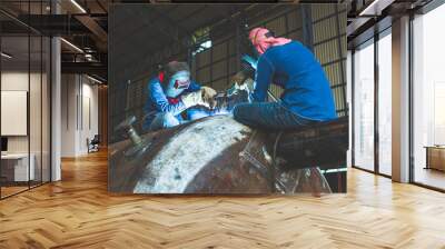 Welding two male worker metal is part in machinery nozzle tank construction Wall mural