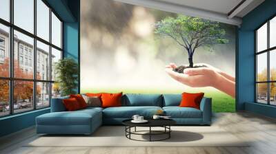 World environment day concept: Human hands holding big tree over blurred nature background Wall mural