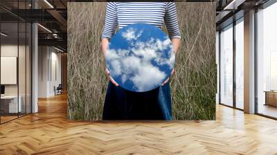 Surrealism with a woman holding a mirror and covering her face in the field with a transparent background behind the mirror Wall mural