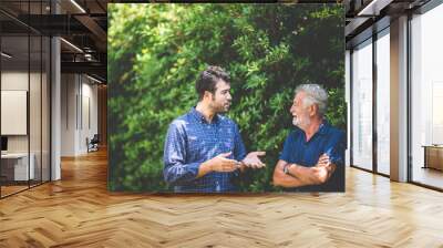 An adult hipster son and senior father talking at home, morning nature scene in the home garden outdoor Wall mural