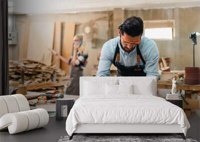 Carpenter working with electric planer on wooden plank in workshop. Craftsman makes own successful small business, man using tool in carpenter's shop to making a furniture from wood Wall mural