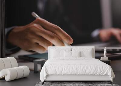 Closeup of hands of a successful business man and entrepreneur in formal clothing sitting in modern lighted office while holding pen and using digital tablet and reading document and making edits Wall mural