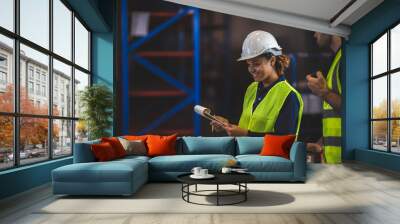 Group of warehouse workers logistic team  wearing hardhats working in aisle between tall racks with packed goods Wall mural